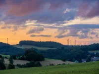 Ausblick auf eine Landschaft bei Sonnenaufgang mit Windrädern und einigen Häusern im Hintergrund