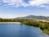 Panorama-Ansicht eines Badesees, mit Wald und Hügel im Hintergrund.