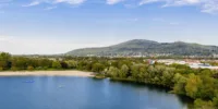 Panorama-Ansicht eines Badesees, mit Wald und Hügel im Hintergrund.