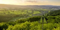 Blick über grüne Landschaft mit Schild Warnung im Vordergrund