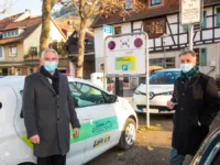 Zwei Menschen stehen an einem Auto vor einem Fachwerkhaus.