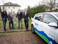 Vier Männer in Anzügen stehen naben einer Ladesäule und einem Elektroauto. Ein Mann hält ein Ladekabel in Händen.