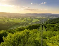 Blick über grüne Landschaft mit Schild Warnung im Vordergrund