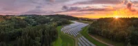 Solaranlagen auf einer grünen Wiese, zwischen Wäldern. Bewölkter Himmel mit einem Sonnenuntergang.