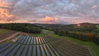 Eine große Solaranlage mit mehreren Reihen von Solarpaneelen, die sich über ein weites, grünes Feld erstrecken